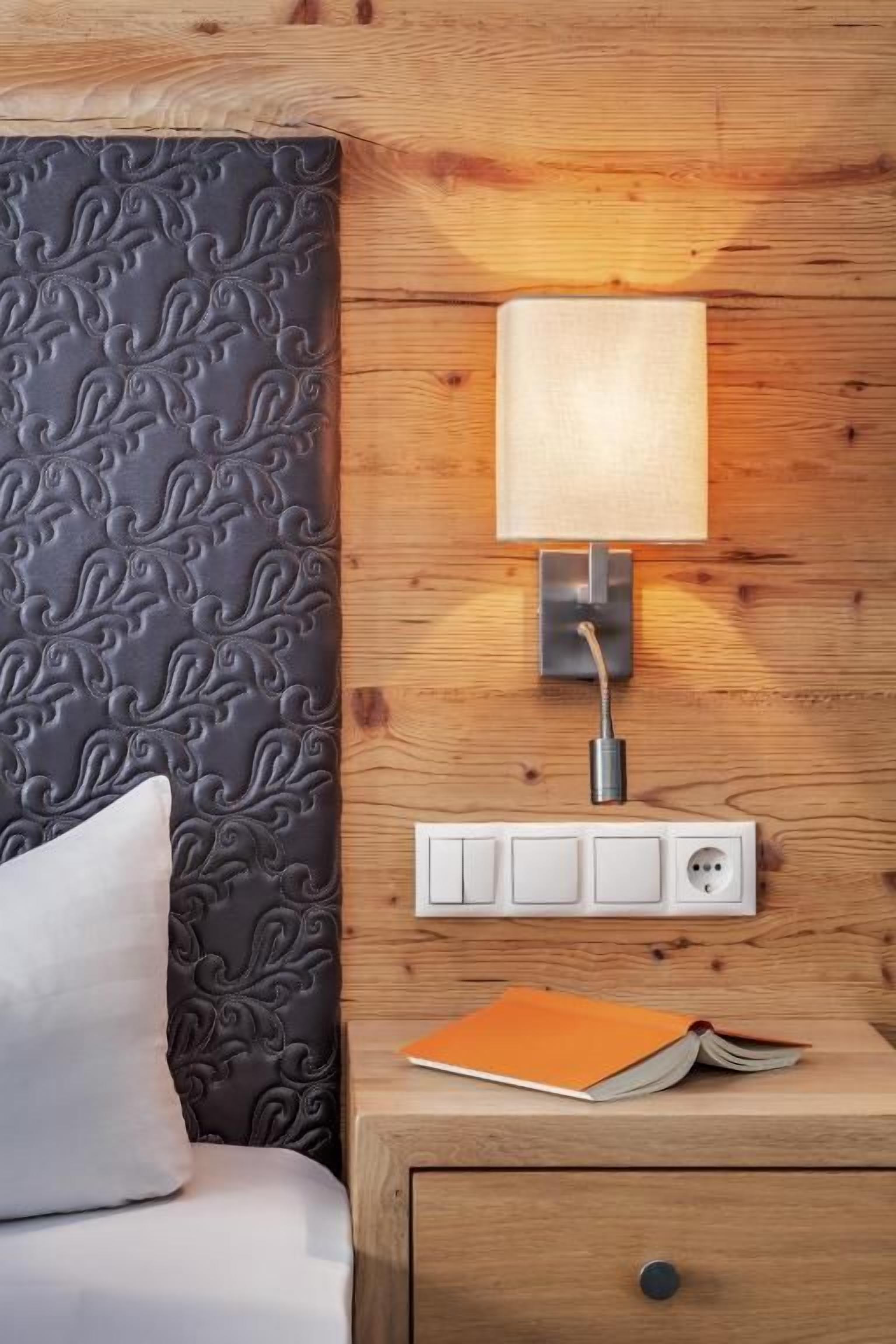 Une tête de lit en bois avec un motif texturé, une lampe de chevet, une prise électrique et un tiroir contenant un livre.