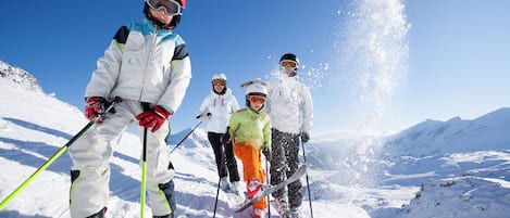 A group of skiers on a snowy slope with clear skies and mountains in the background.