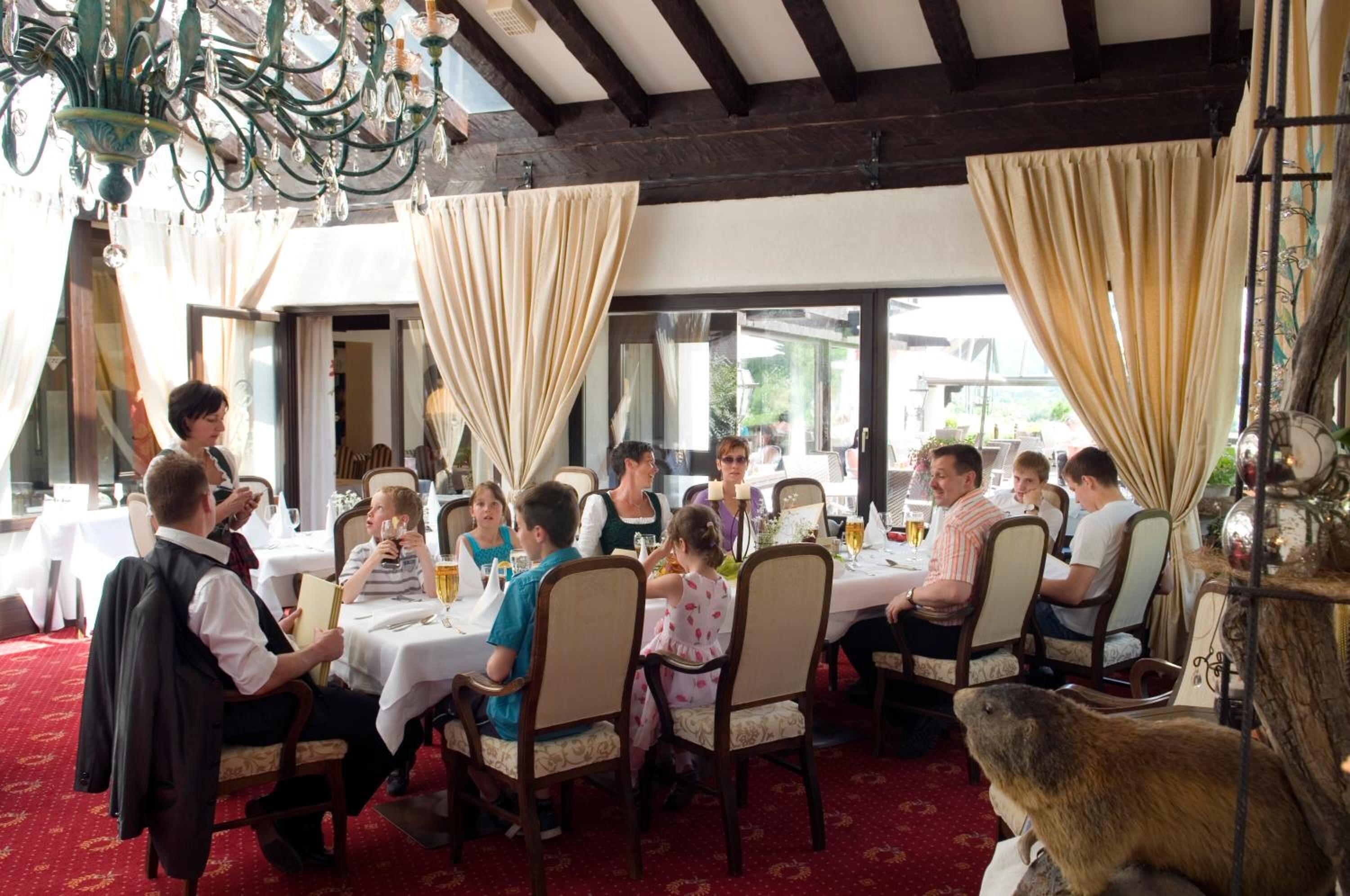 A restaurant with round tables, people dining, and a chandelier.