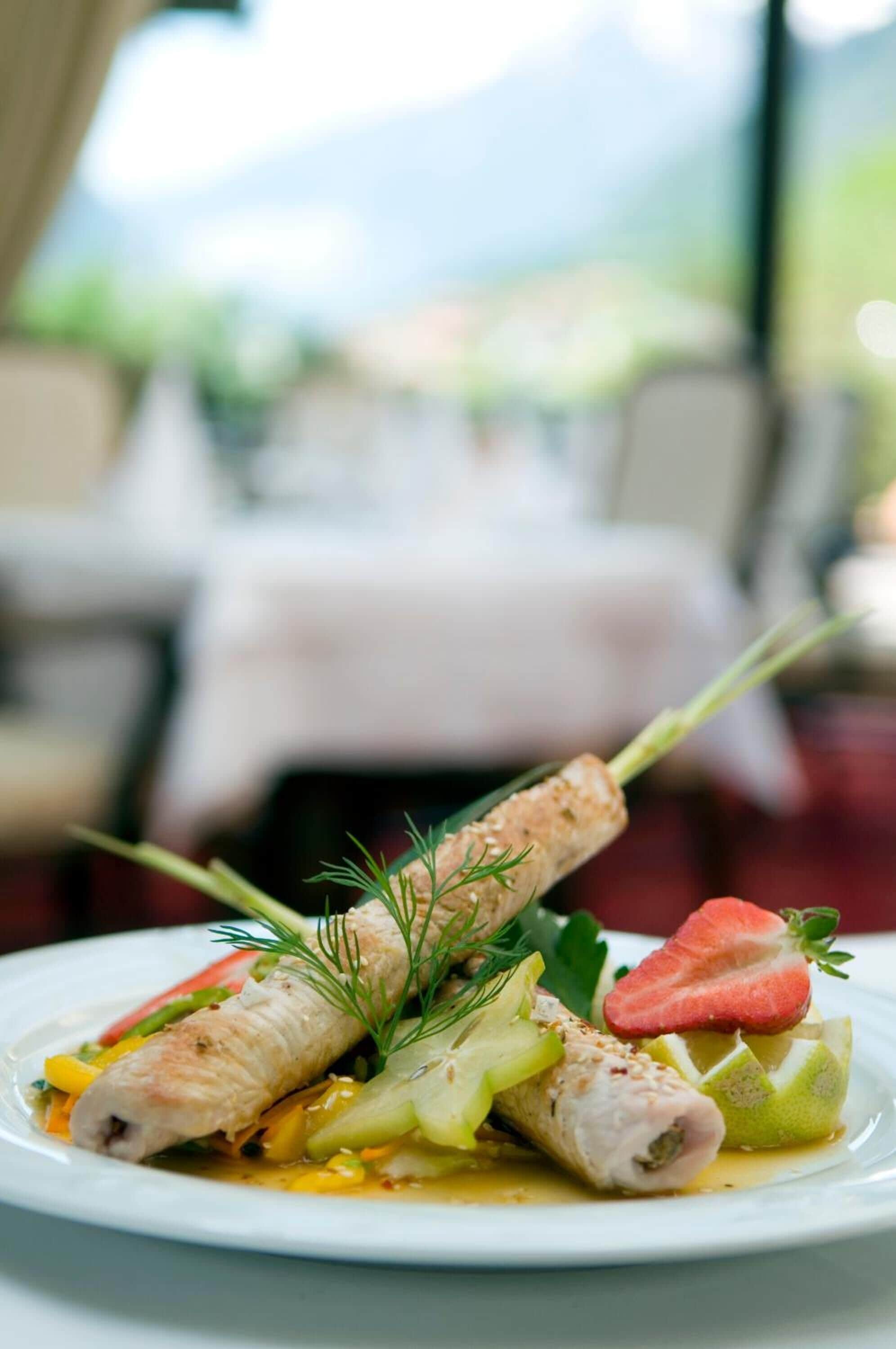 A plate of food with a rolled fish, vegetables, and a strawberry garnish.