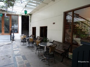 An outdoor cafe area with tables and chairs, a staircase, and a view of a garden. - Malate Pensionne (Manila)