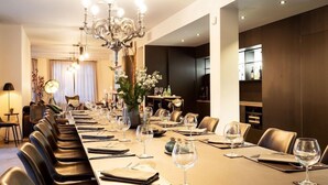 A formal dining room with a long table set for a meal, surrounded by leather chairs, and a chandelier above.