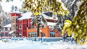 A multi-story building with a red and orange facade, surrounded by snow-covered trees.