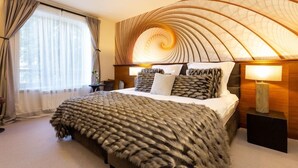 A modern hotel room with a large bed, a curved ceiling design, and a view of the outdoors through the window.
