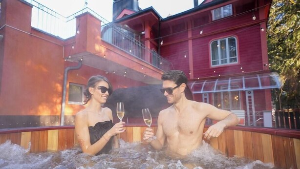 A couple in a hot tub with a red building in the background.