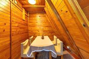 A wooden cabin with a dining table set for four, a ceiling light, and a sloped ceiling. - Villa Yagoda (Samokov)