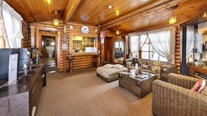 Interior de una cabaña de troncos con una mesa de recepción, mobiliario de mimbre y techo de madera.