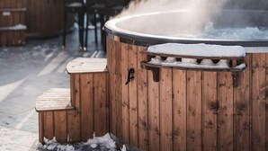 Un jacuzzi con revestimiento de madera, rodeado de suelo y árboles cubiertos de nieve.