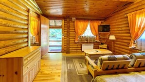 Habitación tipo cabaña de madera con piso de madera, cama, escritorio, silla, televisor y ventana con cortinas.