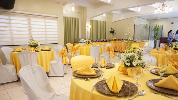 A banquet hall with round tables covered in yellow tablecloths and white chairs, each adorned with yellow sashes. - Stonehouse Bed and Breakfast (Quezon City)