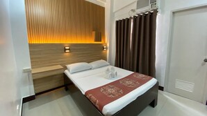 A hotel room with a bed, a wooden headboard, a wall-mounted light fixture, a window with curtains, and a door. - Stonehouse Bed and Breakfast (Quezon City)