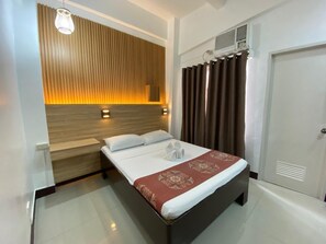 A hotel room with a bed, a wooden headboard, a wall-mounted light fixture, a window with curtains, and a door. - Stonehouse Bed and Breakfast (Quezon City)