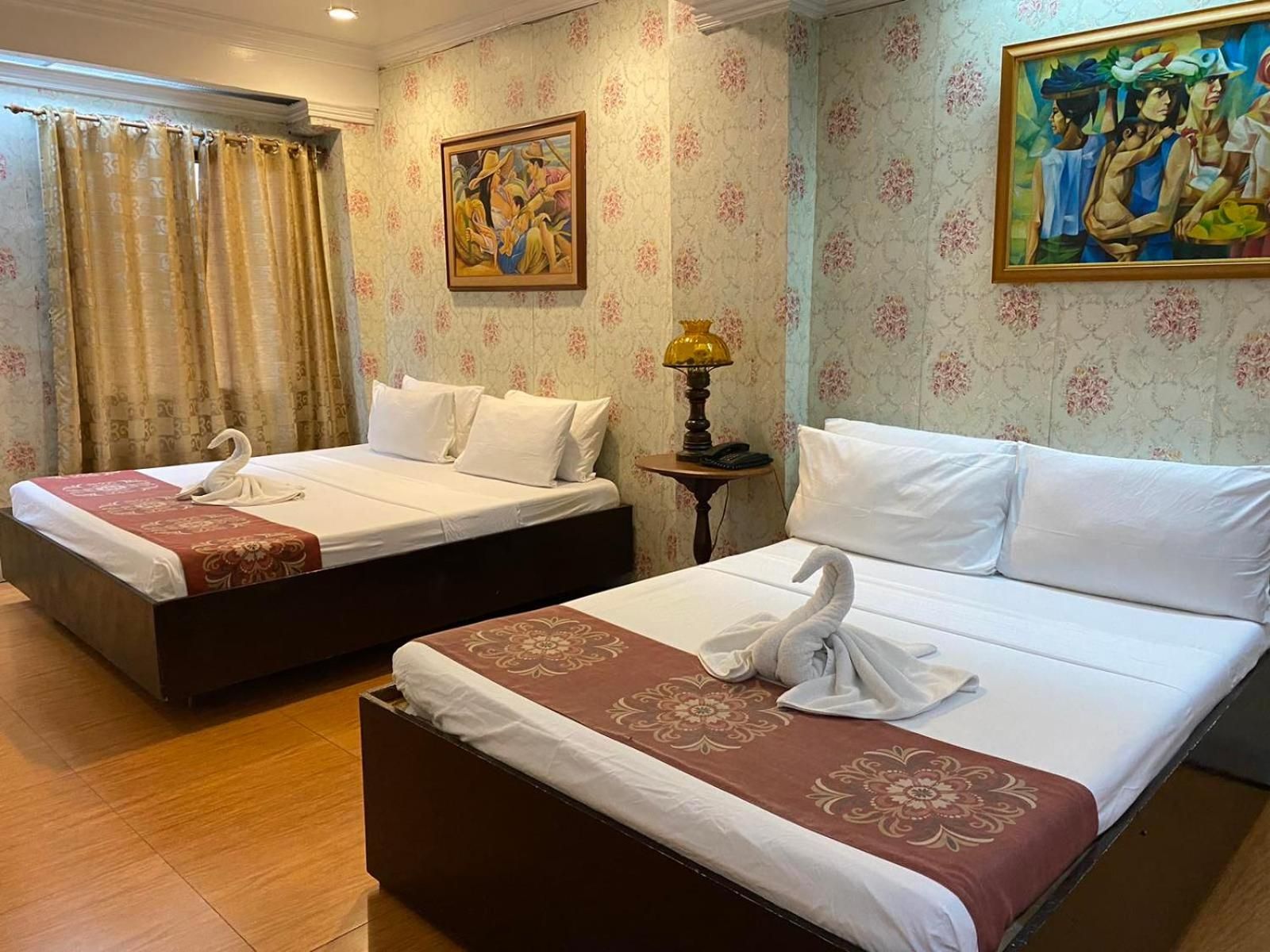 A hotel room with two beds, each with a swan-shaped towel, a lamp on a side table, and floral wallpaper.