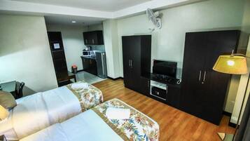 Quarto de hotel com duas camas, uma kitchenette, uma televisão e uma escrivaninha.
