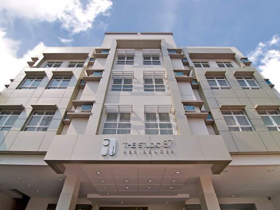 A multi-story hotel with a modern architectural design, featuring a prominent entrance with a sign reading "The Studio 87 Residences".