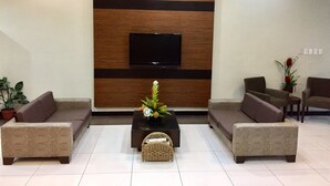 A modern living room with a flat-screen TV mounted on a wooden wall, two sofas, a coffee table with a vase, and a potted plant. - The Studio 87 Residences (Quezon City)