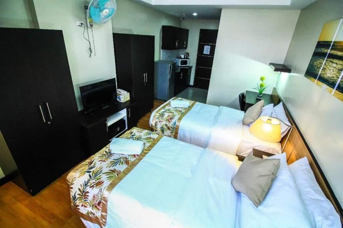 A hotel room with two beds, a desk, a chair, a TV, a microwave, and a small kitchenette.
