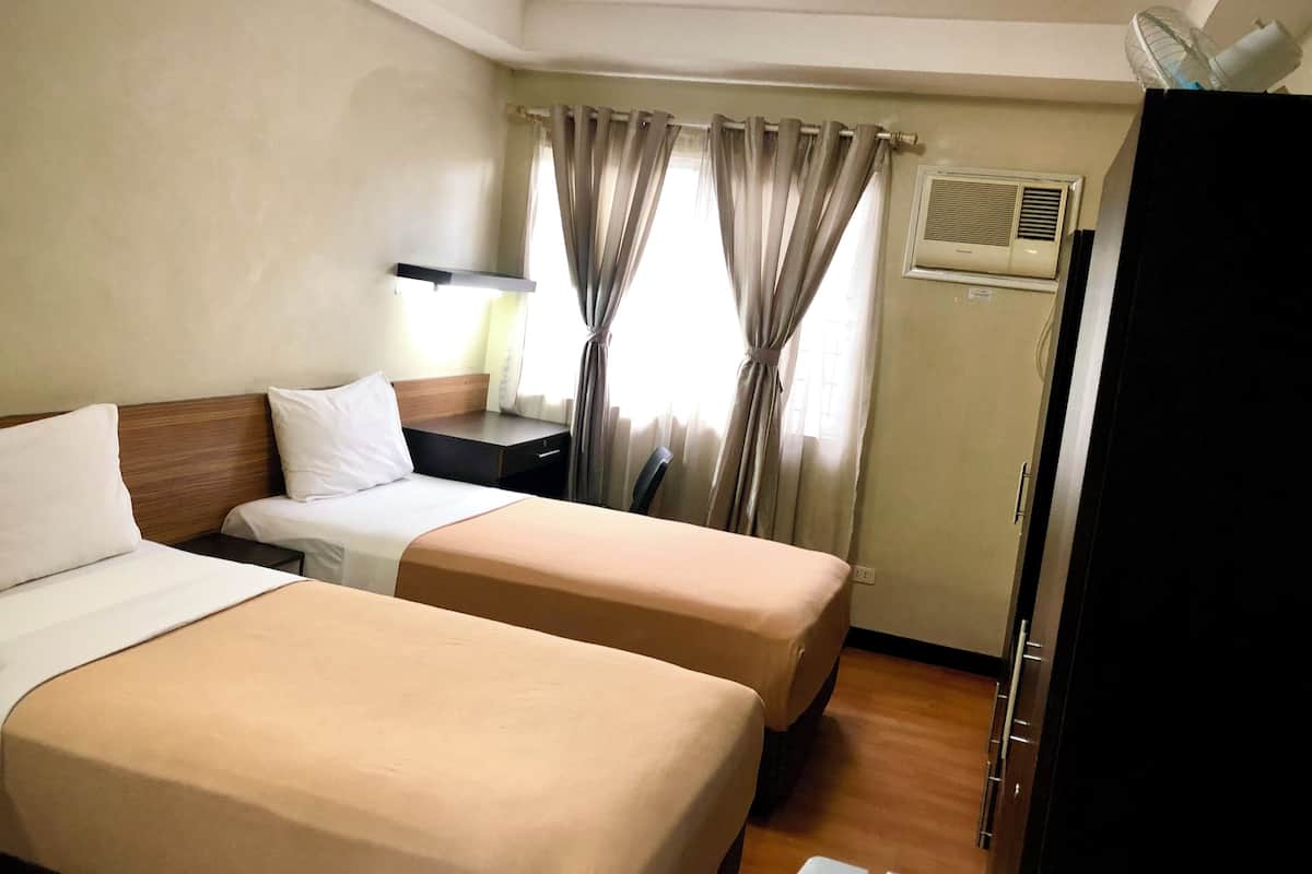 A hotel room with two beds, a nightstand, a lamp, an air conditioning unit, and a wardrobe.