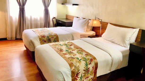 A hotel room with two beds, a desk, a chair, a lamp, and a window with curtains. - The Studio 87 Residences (Quezon City)