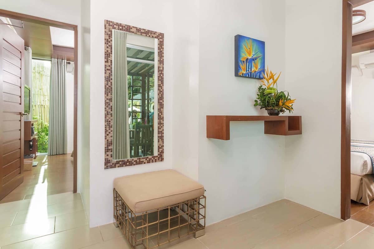 A clean, modern hallway with a bench, a mirror with a decorative frame, a wall-mounted shelf with a plant, and a door leading to a balcony.