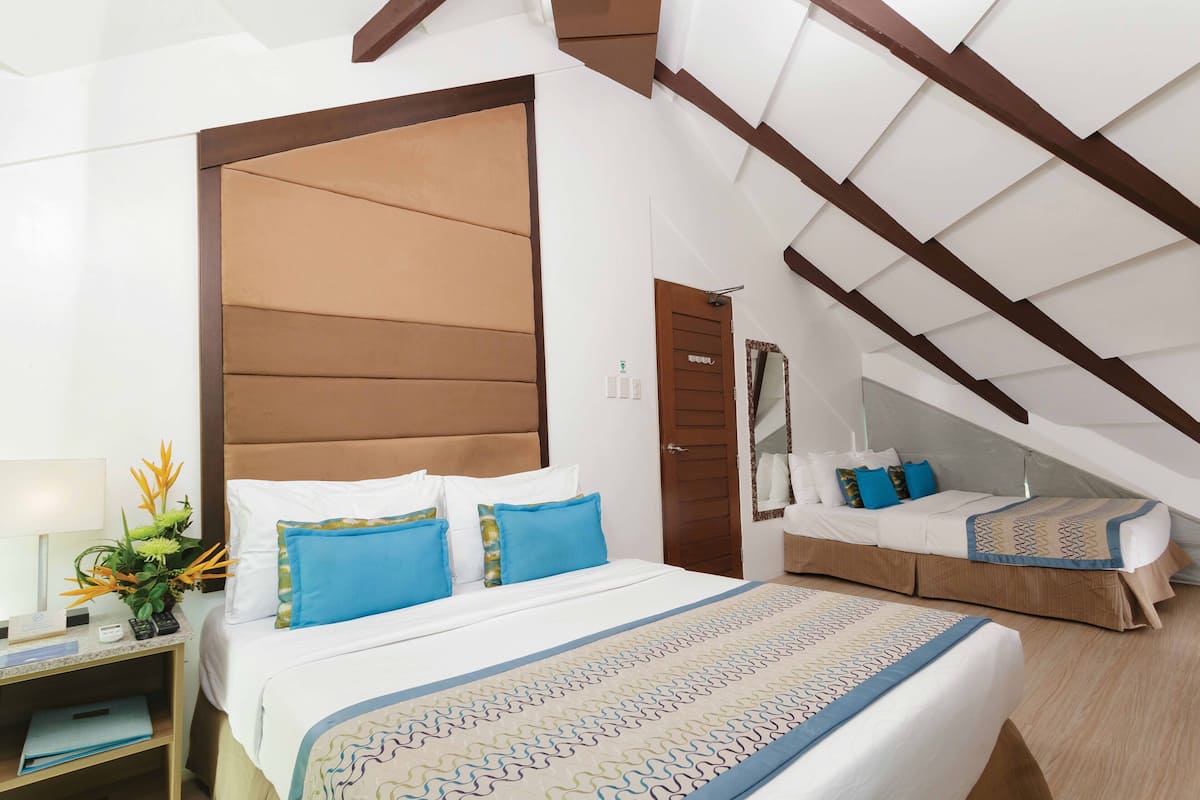 A hotel room with a large bed, a smaller bed, a nightstand, a mirror, and a ceiling with wooden beams.
