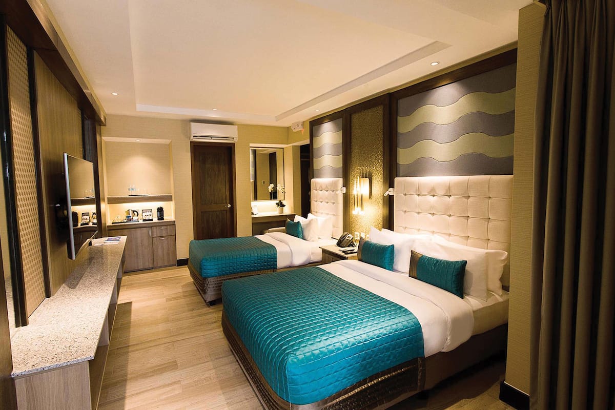 A hotel room with two beds, a sitting area, a vanity, and a television.