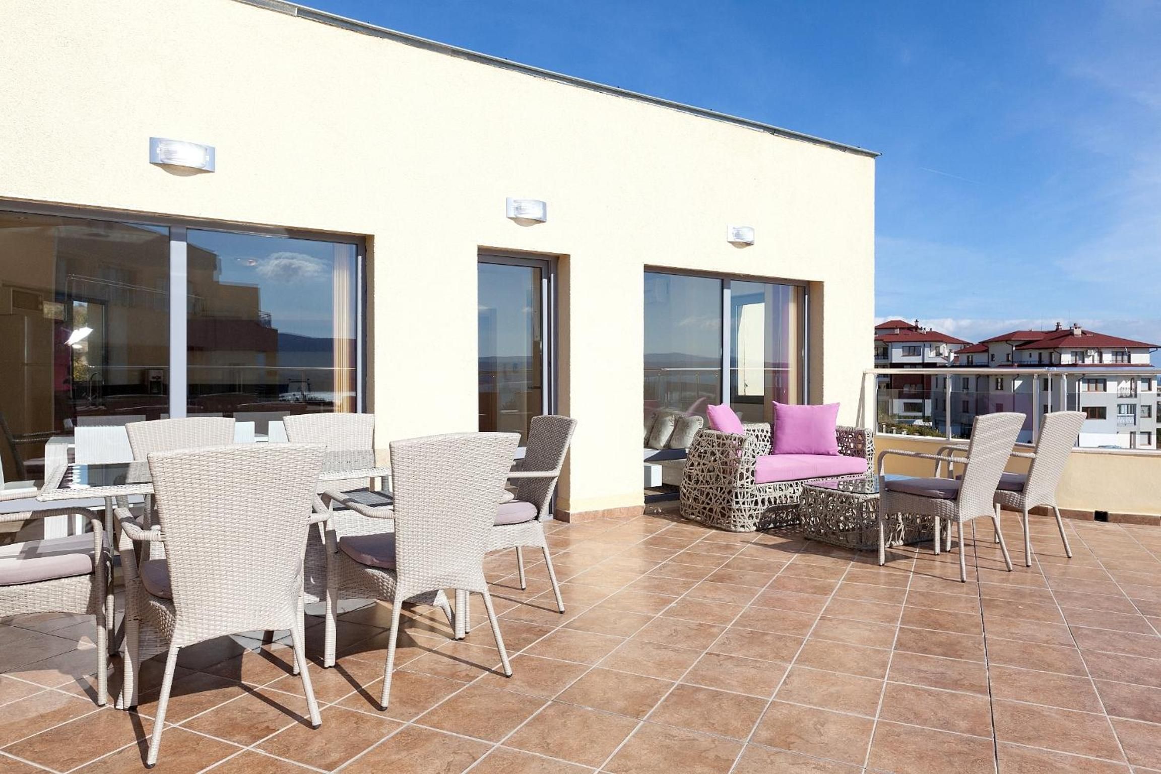 A terrace with outdoor furniture, large windows, and a view of the city.
