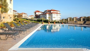 A swimming pool with lounge chairs and a building with red roofs in the background. - Byala Panorama Resort (Byala)