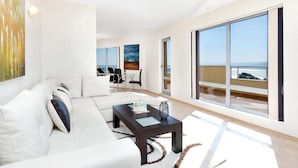 A modern living room with a white sofa, a coffee table, and a view of the sea through large windows. - Byala Panorama Resort (Byala)