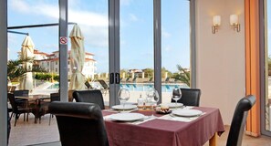 A dining area with a table set for two, overlooking a pool and buildings.