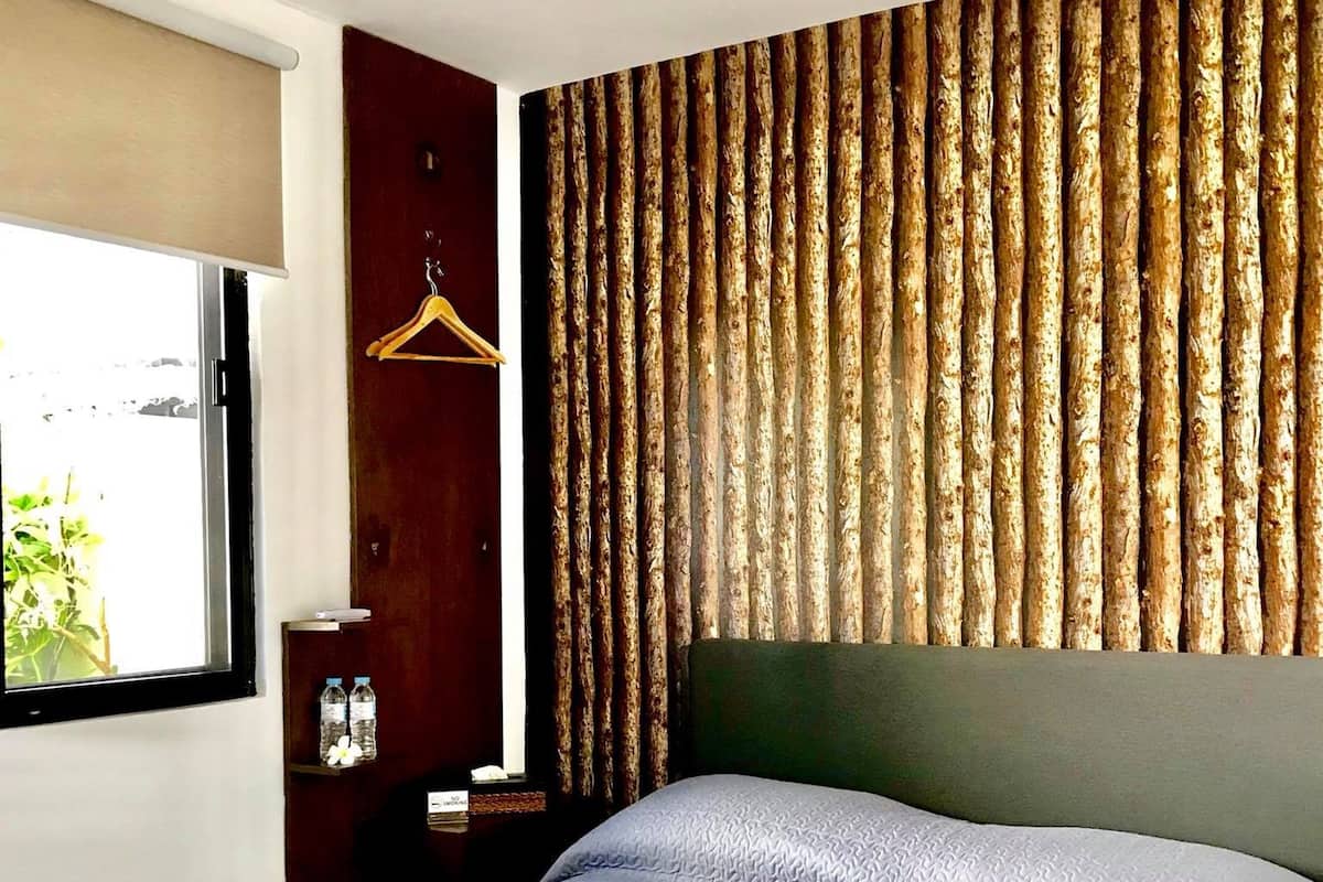 A hotel room with a large bed, a wooden headboard, a window with a view, and a small nightstand with a bottle and a tissue box.