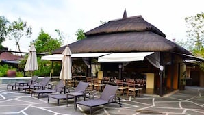 A covered outdoor seating area with lounge chairs and umbrellas, a thatched-roof structure, and a pool in the background. - Segara Villas (Olongapo)