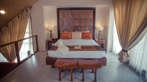 A hotel room with a large bed, wooden headboard, two bedside tables with lamps, a bench at the foot of the bed, and a view through the window. - Segara Villas (Olongapo)