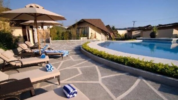 A pool area with lounge chairs and umbrellas, surrounded by a landscaped garden and a pool. - Segara Villas (Olongapo)
