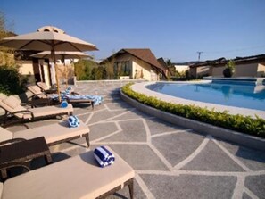 A pool area with lounge chairs and umbrellas, surrounded by a landscaped garden and a pool. - Segara Villas (Olongapo)