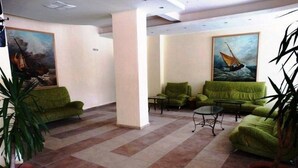 Un hall con sofás verdes, una mesa de centro y plantas en macetas.