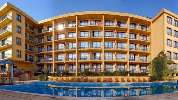 Un hotel de varios pisos con balcones, piscina y un patio con pavimento de baldosas.