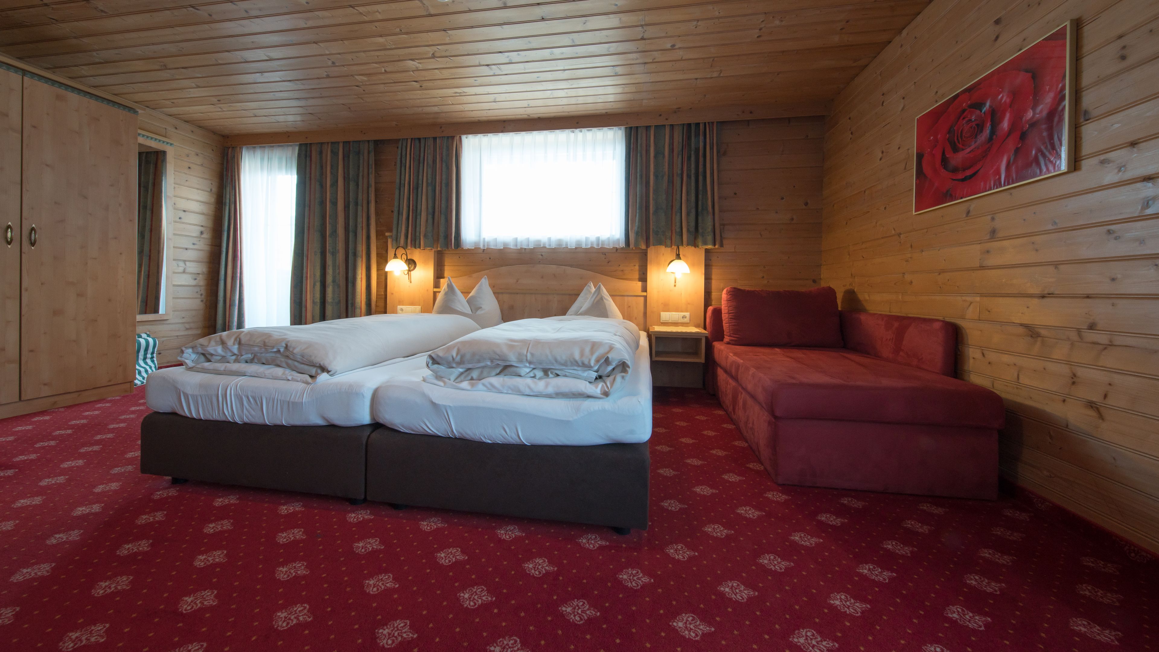 A wooden cabin room with a bed, a red sofa, and a wooden wardrobe.