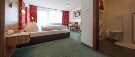 Habitación de hotel con cama, escritorio, silla, baño y vistas al exterior.