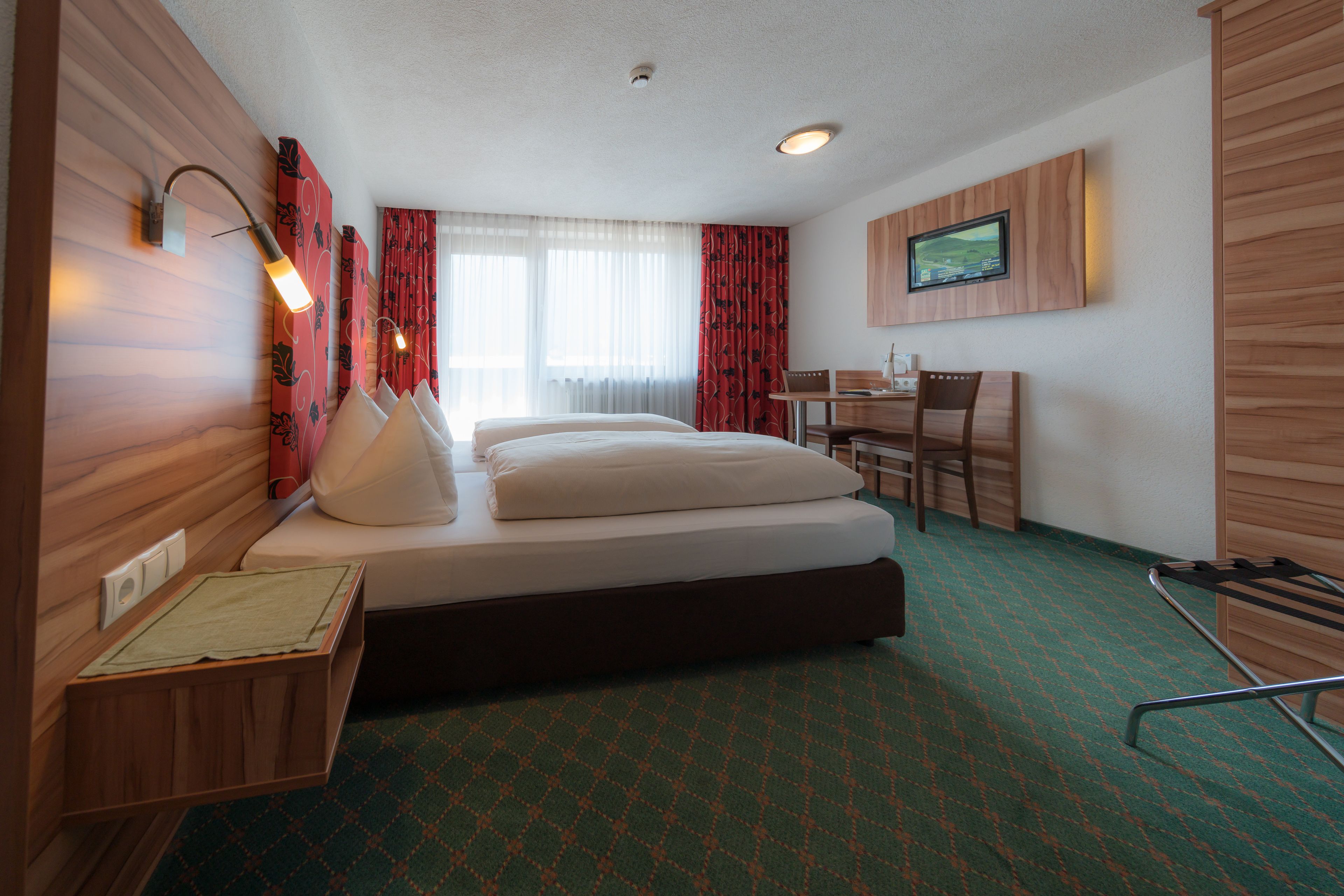 A hotel room with a bed, a desk, a chair, a television, and a window with curtains.