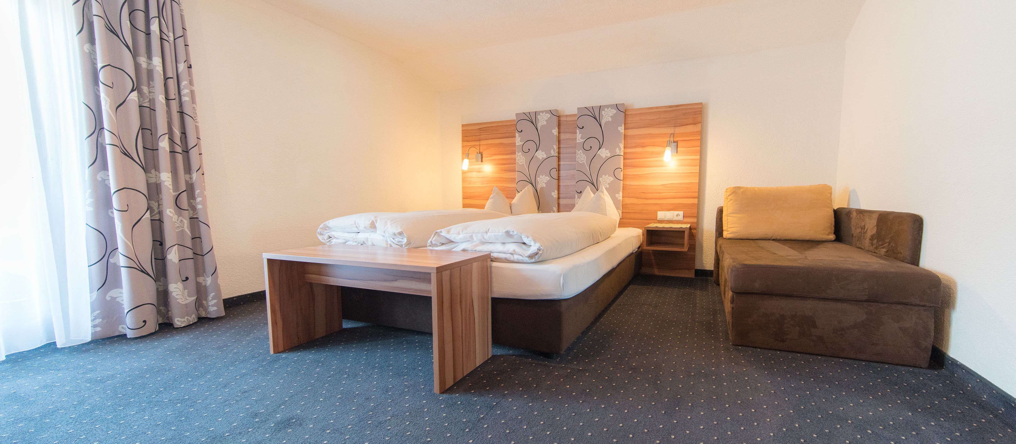 Een hotelkamer met een bed, een kleine tafel, een bank en twee wandlampen.