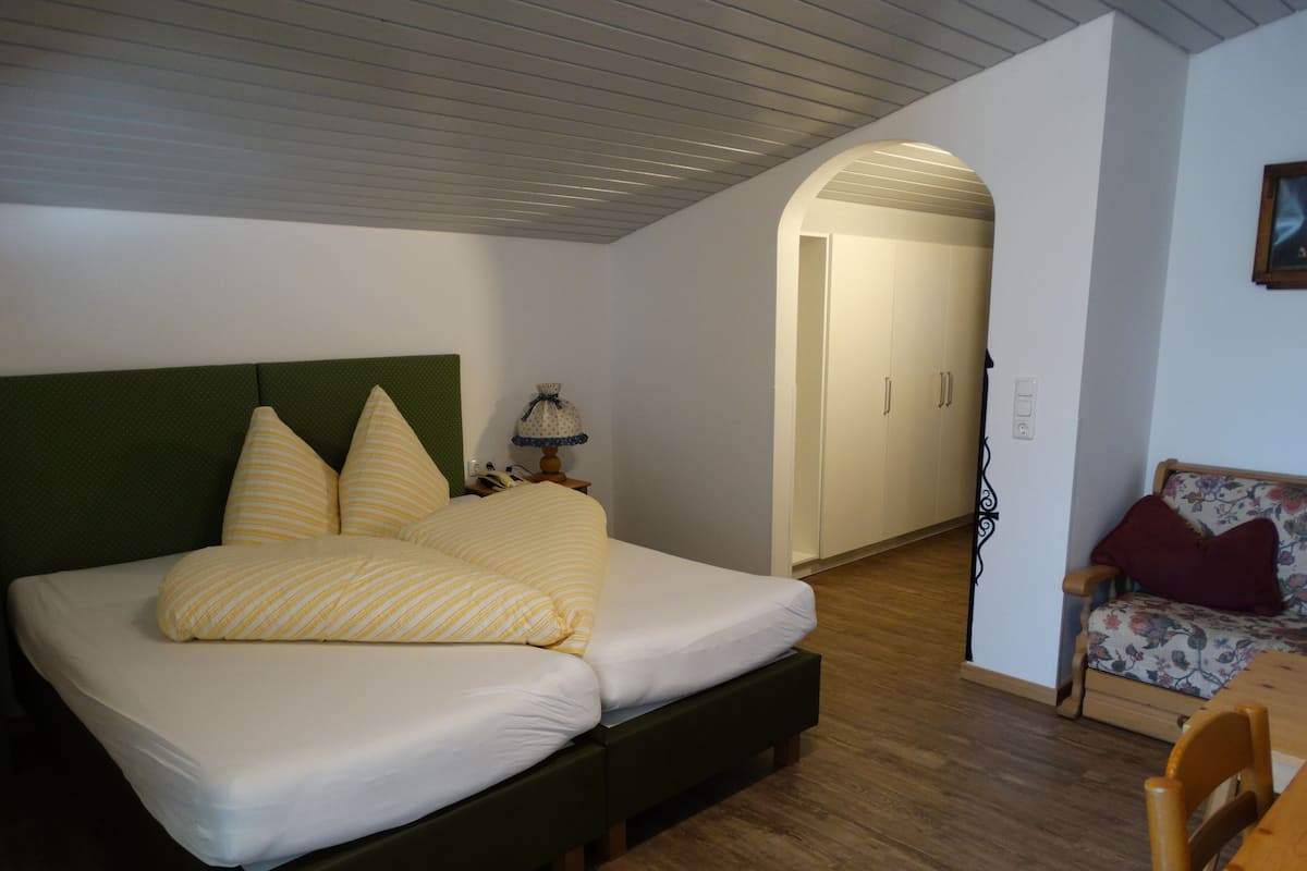 Een slaapkamer met een bed, nachtkastje, lamp, stoel en kledingkast.