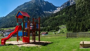 A playground with a trampoline and a slide, surrounded by houses and mountains. - Gasthof Pension Posthansl (Heiterwang)