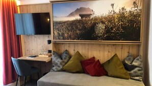 A room with a wooden headboard, a flat-screen TV mounted on the wall, a desk with a chair, and a large framed picture of a landscape. - Gasthof Pension Posthansl (Heiterwang)