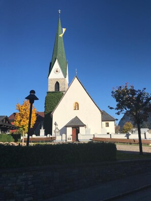 A church with a tall steeple and a clock, surrounded by a stone wall and benches. - Hotel Thaler (Thiersee)