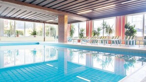 An indoor swimming pool with clear blue water, surrounded by windows and potted plants. - Hotel Thaler (Thiersee)
