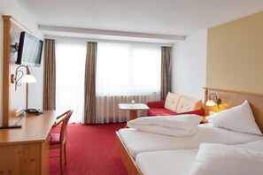 A hotel room with a bed, a desk with a telephone, a TV, a small table, and a sofa. - Hotel Thaler (Thiersee)