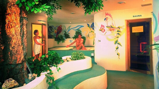 A spa area with a bathtub, a sauna, and a mural of a parrot. - Hotel Thaler (Thiersee)
