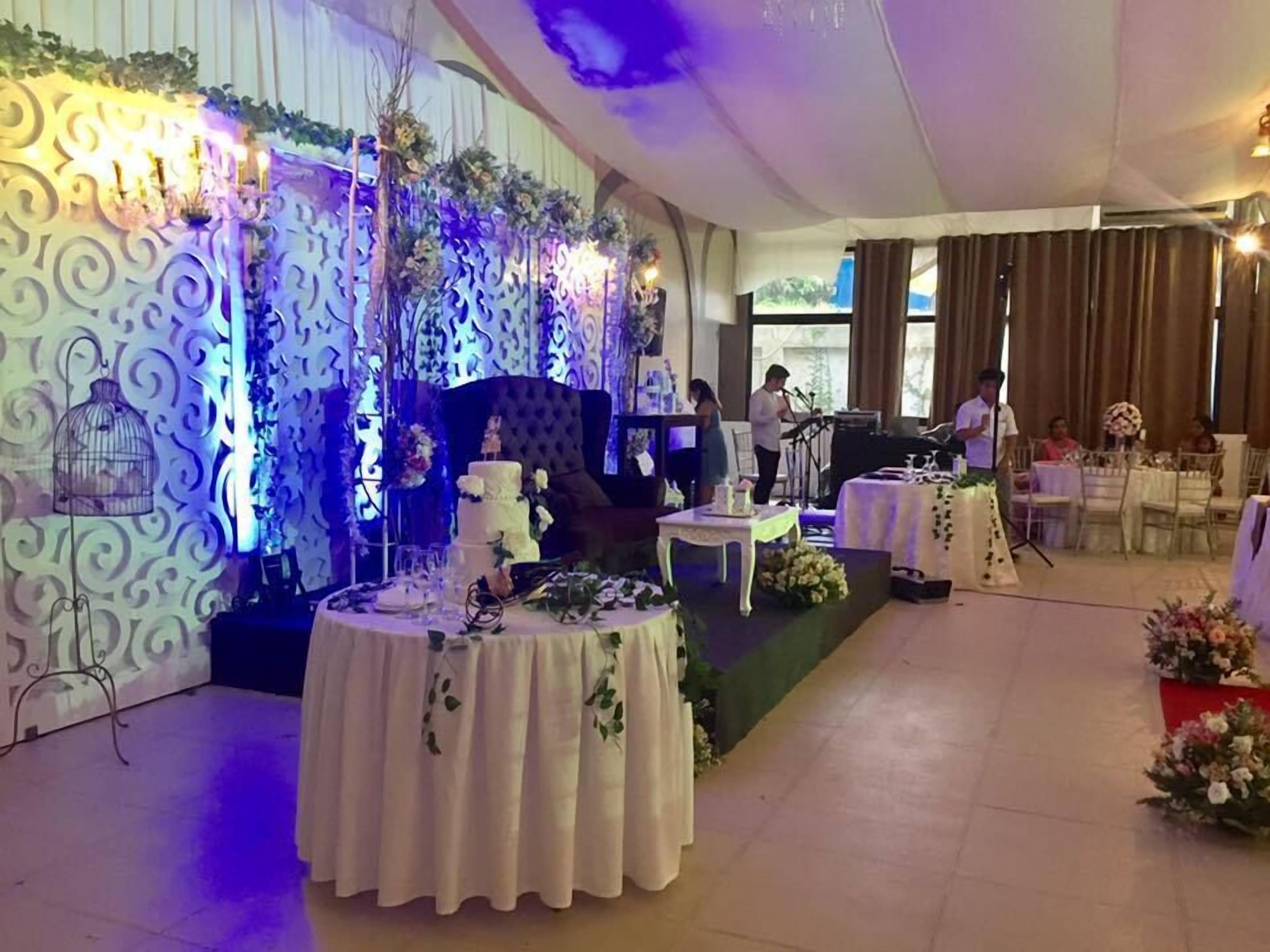 A wedding reception with a decorated stage, tables with floral centerpieces, and a DJ booth.