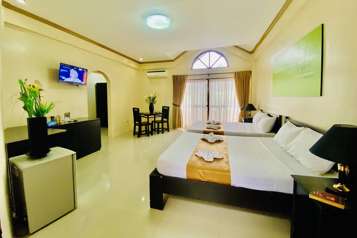 A hotel room with a bed, a desk, a TV, and a dining area.